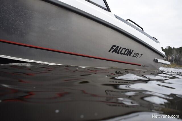 A close-up of the FALCON BR 7 boat, partially submerged in water with a forest background. Visible reflections on the water surface.